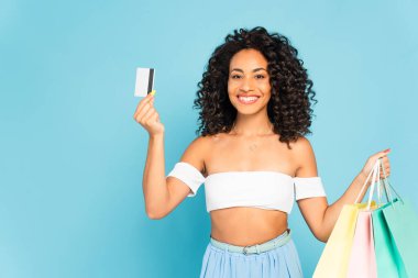 Neşeli Afrikalı Amerikalı kadın kredi kartı ve alışveriş torbaları tutuyor. 