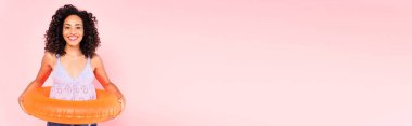 Yüzme yüzüğüyle pembe üzerinde duran gülümseyen Afrikalı Amerikalı kadının panoramik çekimi. 