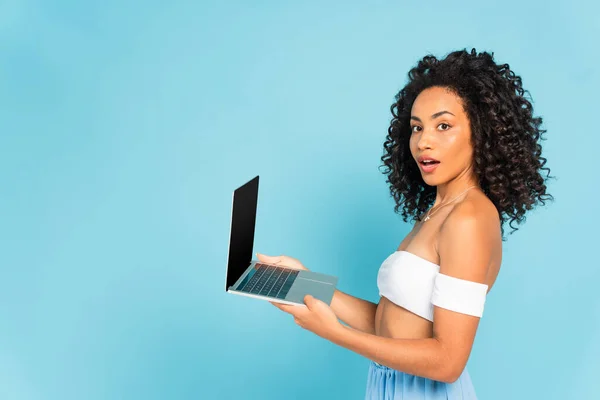 Έκπληκτος Και Σγουρά Αφροαμερικανή Γυναίκα Κρατώντας Φορητό Υπολογιστή Απομονωμένο Μπλε — Φωτογραφία Αρχείου