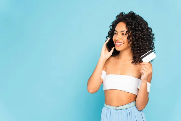 快乐的非洲裔美国女人拿着信用卡 用蓝色隔离的智能手机交谈 — 图库照片