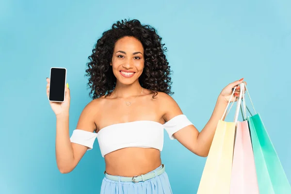 Усміхнена Афроамериканка Тримає Сумки Покупок Смартфон Порожнім Екраном Ізольовано Синьому — стокове фото