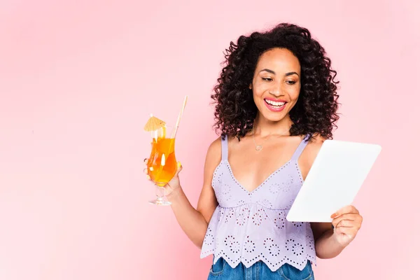 快乐的非洲裔美国女孩拿着鸡尾酒 看着用粉色隔离的数码平板电脑 — 图库照片