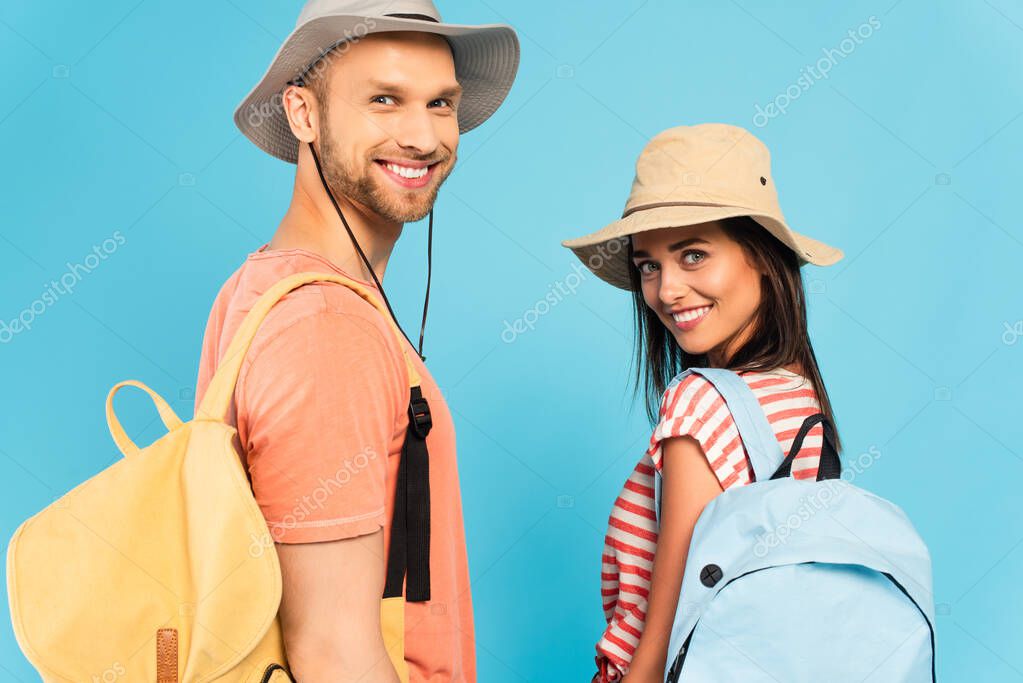happy travelers in hats looking at camera isolated on blue