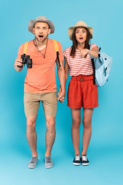 Şok olmuş şapkalı kadın parmağıyla neredeyse şaşırmış erkek arkadaşını işaret ediyor mavi dürbünlü dürbünle. 