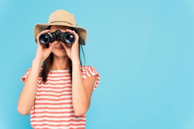 young woman in hat looking through binoculars isolated on blue clipart
