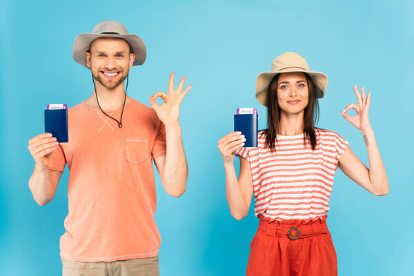 happy man and woman in hats holding passports and showing ok sign on blue