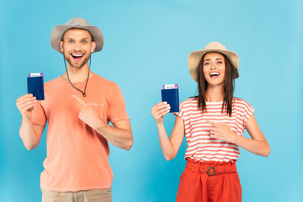 happy man and woman in hats pointing with fingers at passports on blue