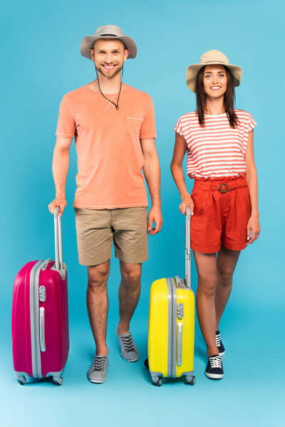 happy couple in hats standing near travel bags on blue 