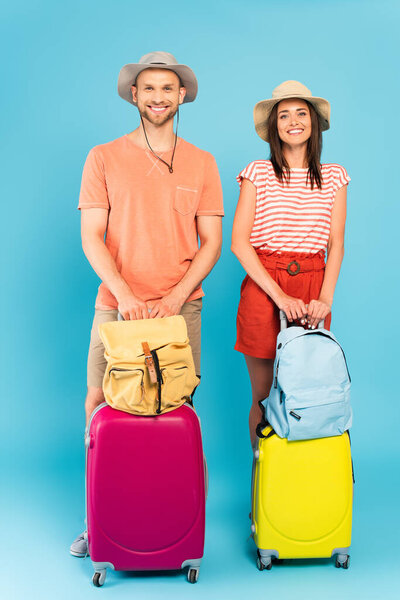 happy couple in hats standing with luggage and backpacks on blue 