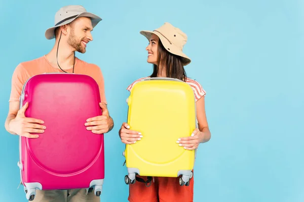 Casal Feliz Olhando Para Outro Segurando Bagagem Isolada Azul — Fotografia de Stock