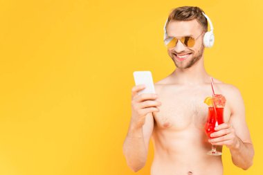 Güneş gözlüklü, neşeli ve üstsüz bir adam akıllı telefon kullanıyor. 