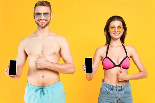 戴着太阳镜 身穿泳衣 手持装有空白屏幕的智能手机 大拇指被黄色隔开的快乐夫妻 — 图库照片