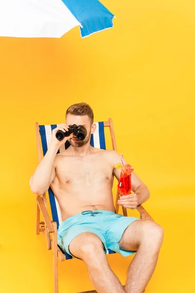 Shirtless Man Holding Cocktail Looking Binoculars While Sitting Deck Chair — Stock Photo, Image