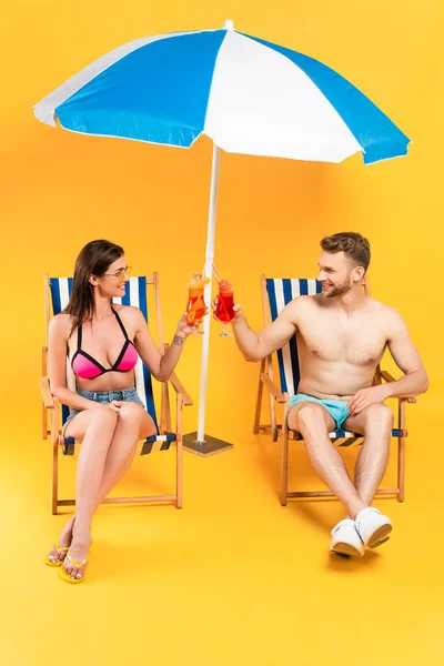 Cheerful Couple Clinking Cocktails Sitting Deck Chairs Beach Umbrella Yellow — Stock Photo, Image