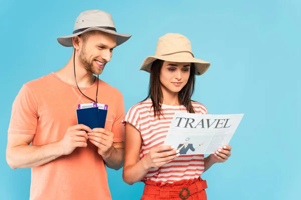 戴帽子的快乐男人拿着护照 身边的飞机票 正在看一份蓝色的旅行报纸 — 图库照片