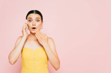Şok olmuş esmer, genç bir kadın. Pembelerden izole bir şekilde akıllı telefondan konuşuyor.