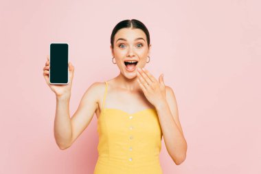 Heyecanlı esmer kadın elinde pembe ekranlı akıllı telefon tutuyor.