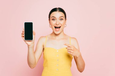 Heyecanlı esmer kadın pembe ekranda boş ekranlı akıllı telefonu işaret ediyor.