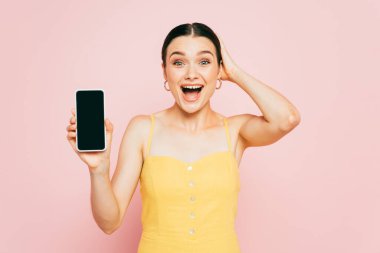 Heyecanlı esmer kadın elinde pembe ekranlı akıllı telefon tutuyor.