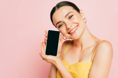 Kumral genç bir kadın pembe ekranda boş ekranlı akıllı telefon tutuyor.