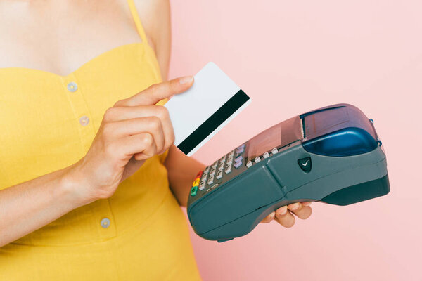 cropped view of woman using credit card and payment terminal isolated on pink