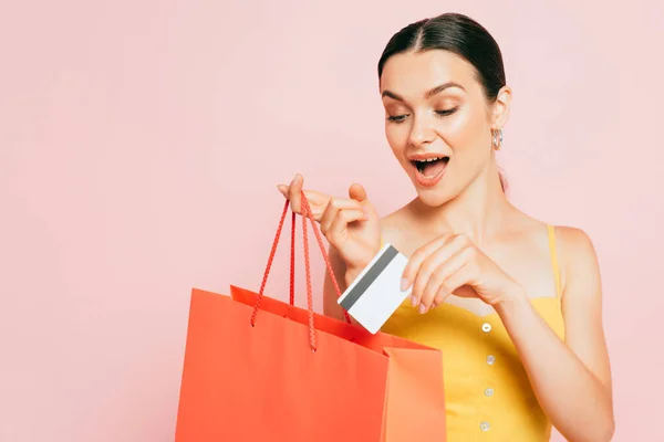 興奮ブルネット若い女性置くクレジットカードでショッピングバッグ孤立でピンク — ストック写真