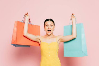 excited brunette young woman with shopping bags in raised hands on pink clipart