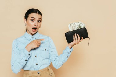 Şok olmuş esmer kadın kot gömlek içinde cüzdanı işaret eden bej renkli dolarlarla