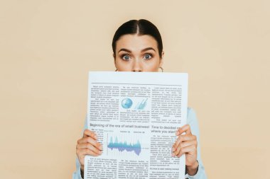 Şok olmuş esmer kadın kot gömlekli, elinde iş gazetesi olan bej rengi bir elbiseyle, yüzünün önünde soyutlanmış.