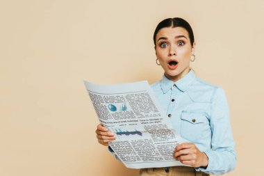 Şok olmuş esmer kadın kot gömlekli, iş gazetesi bej renkli.