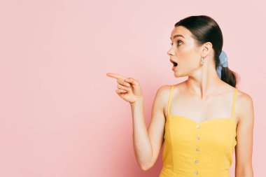 shocked brunette young woman pointing aside on pink clipart