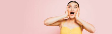 shocked brunette young woman holding head on pink, panoramic shot clipart