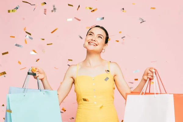 Brunette Jonge Vrouw Met Boodschappentassen Onder Vallen Confetti Geïsoleerd Roze — Stockfoto