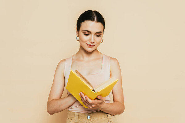 брюнетка молодая женщина читает желтую книгу изолированы на бежевый