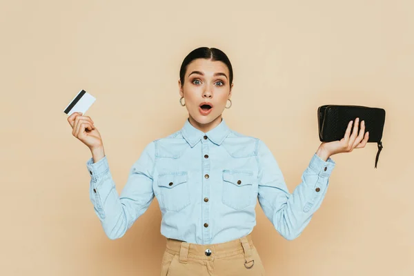 Mujer Morena Impactada Camisa Mezclilla Sosteniendo Billetera Tarjeta Crédito Aislada —  Fotos de Stock