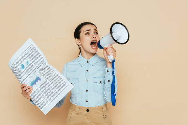 brunette woman in denim shirt with newspaper screaming in loudspeaker isolated on beige