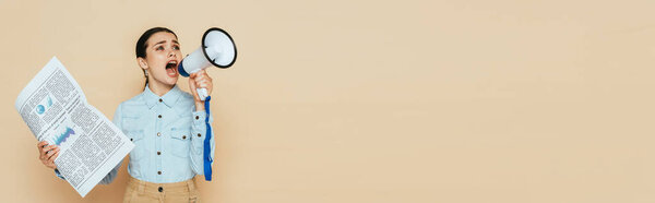 brunette woman in denim shirt with newspaper screaming in loudspeaker isolated on beige, panoramic shot