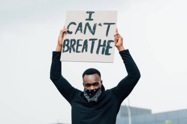 african american man looking at camera and holding placard with i cant breathe lettering outside  clipart