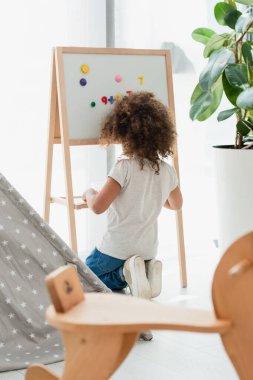 Manyetik sehpanın yanında mıknatıslarla oturan kıvırcık saçlı Afrikalı Amerikalı çocuk. 