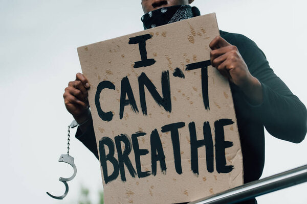 cropped view of handcuffed african american man holding placard with i cant breathe lettering outside 