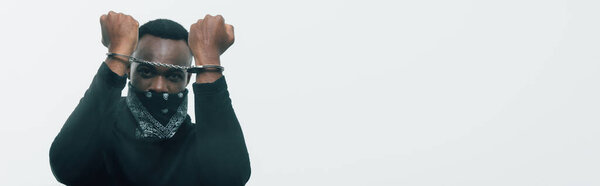 Panoramic shot of handcuffed african american man looking at camera isolated on white, racism concept