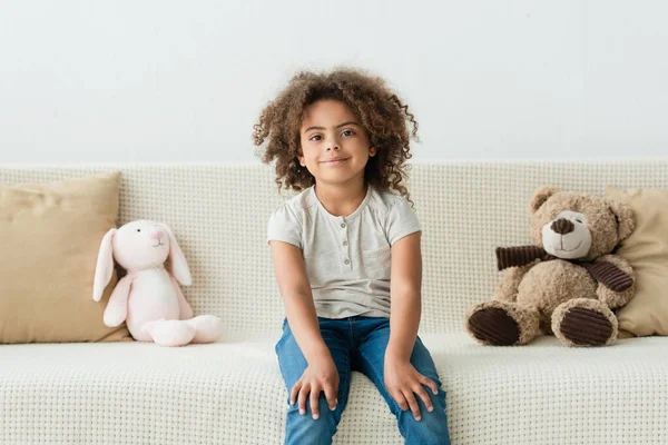 Кучерява Афроамериканська Дитина Дивиться Камеру Сидить Дивані Якими Іграшками — стокове фото
