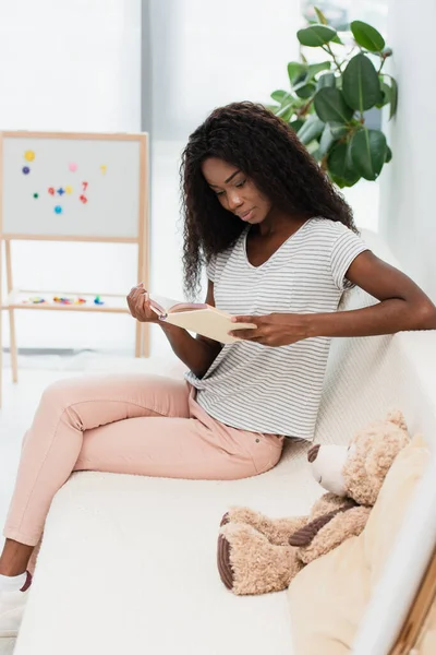 African American Woman Reading Book While Sitting Sofa — Stock Photo, Image