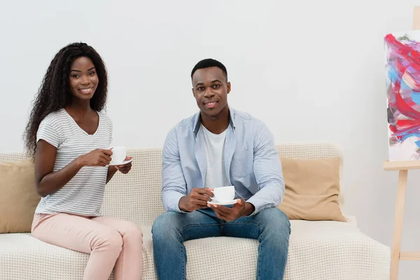 アフリカ系アメリカ人のカップルがコーヒーを持ってソファに座り — ストック写真