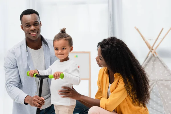 Africano Americano Hombre Mirando Cámara Mientras Madre Tocando Hijo Scooter — Foto de Stock