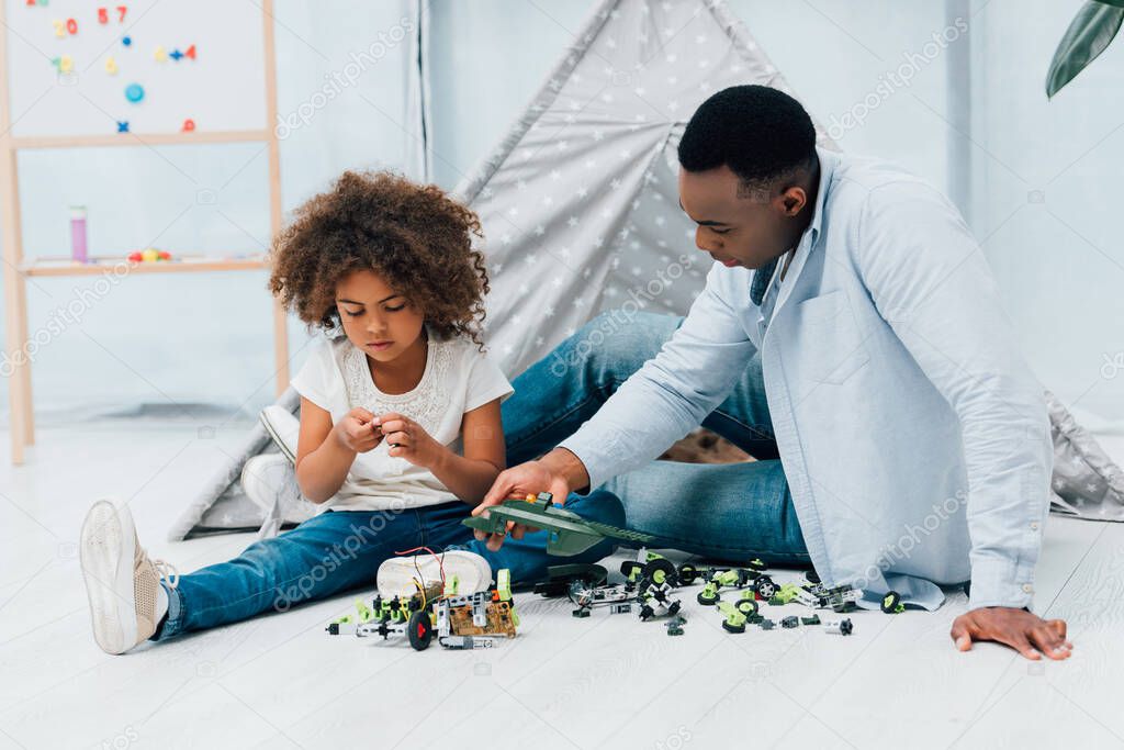 african american father and child sitting on floor and playing with plastic toys 