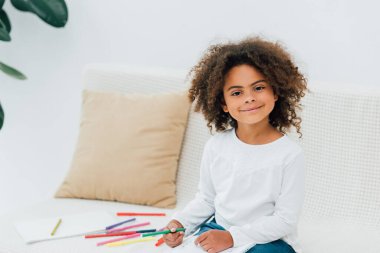 curly african american child holding color pencil and looking at camera  clipart