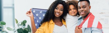 Amerika bayrağıyla kaplanmış Afro-Amerikan ailesinin yatay mahsulü kameraya bakıyor. 