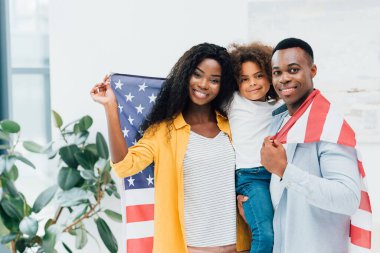 Afro-Amerikan ailesi Amerika bayrağını tutuyor ve kameraya bakıyor. 