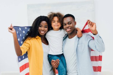Afro-Amerikan ailesi kameraya bakarken Amerika bayrağı tutuyor. 
